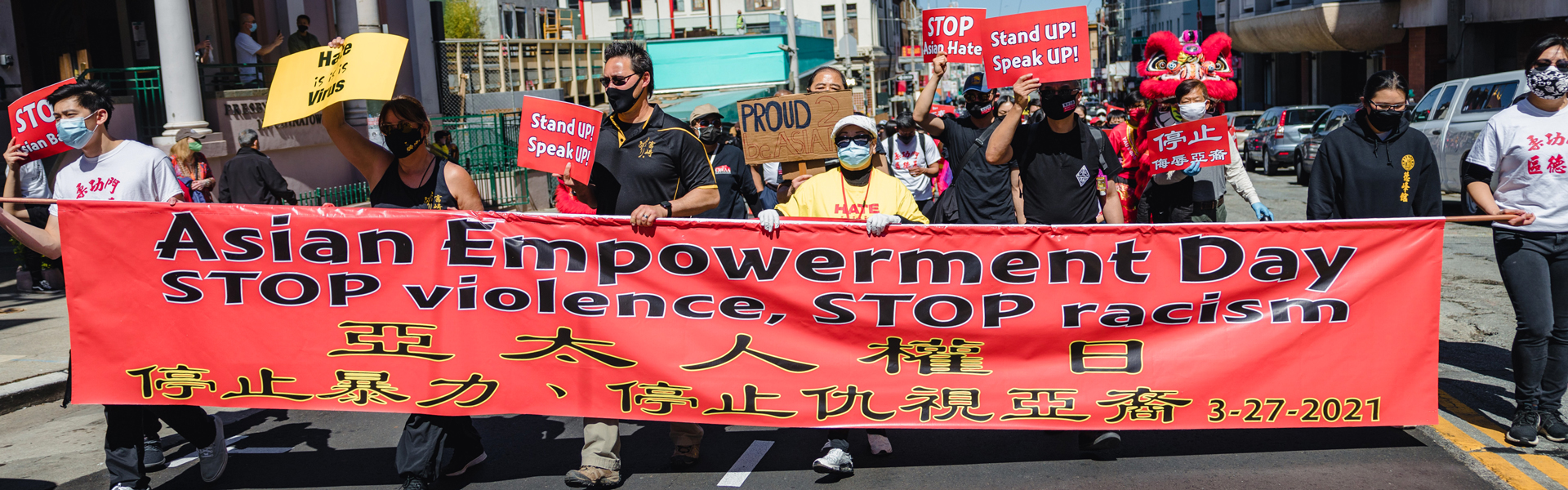 People holding a banner walking down a street "Asian Empowerment Day" Stop the violence, Stop racism.